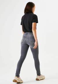 Skinny jeans in donkergrijs denim, hoge taille, met vijf zakken en subtiele stiksels. G gedragen met een zwart T-shirt en beige sneakers.