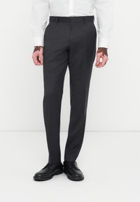 Graue, maßgeschneiderte Hosen aus glattem Stoff. Sie verfügen über einen geraden Bein-Schnitt, Gürtelschlaufen und werden mit schwarzen eleganten Schuhen kombiniert.