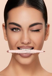 Prodotto per labbra Pupa Creamy Duo, con design a doppia estremità, custodia rosa pallido e una punta a matita leggermente più scura, tenuto in bocca da una modella.