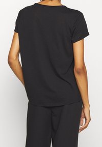 T-shirt nera a maniche corte con scollatura rotonda. Tessuto di cotone morbido e vestibilità rilassata con orlo posteriore leggermente più lungo.