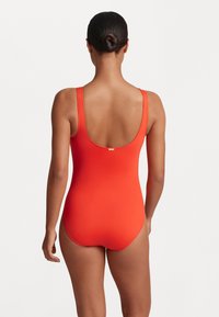 Röd baddräkt i ett stycke med breda axelband, uringad rygg och en slät yta. Har en liten guldfärgad logotyp närmast knäppningen.