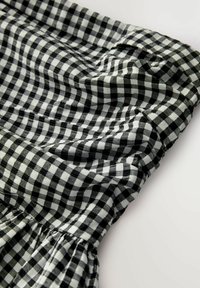 Czarno-biała tkanina w kratkę typu gingham z elastycznym pasem, z plisowanymi detalami i miękką, teksturowaną powierzchnią.
