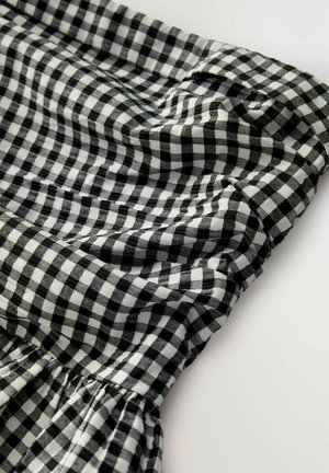 Material gingham alb-negru cu un tiv elastic, prezentând detalii pliate și o suprafață moale, texturată.