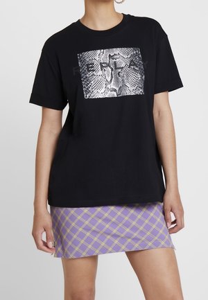 T-shirt oversize noir avec impression serpent argentée et texte "REPLAY", associé à une mini-jupe à carreaux violette et jaune.