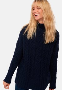 Pull en maille torsadée bleu marine avec col montant, manches longues et ourlet côtelé. Le motif texturé ajoute un intérêt visuel au design.