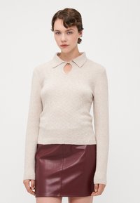 Beige neulepaita, jossa on kaulus ja avausyksityiskohta kaula-aukossa. Yhdistetty burgundin väriseen nahkaminihameeseen.