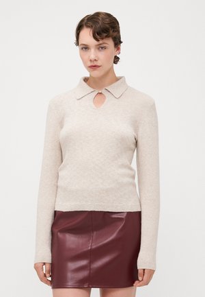 Beige strikket genser med krage, med en åpning ved halsen. Kombinert med et burgunder skinnminiskjørt.