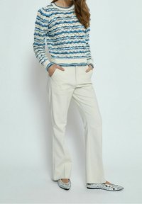 Niebiesko-biały sweter dzianinowy w paski z bufiastymi rękawami, zestawiony z kremowymi spodniami o szerokich nogawkach i srebrnymi balerinami z ćwiekami. Teksturowany materiał z kontrastowym wykończeniem.