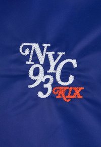 Granatowy materiał ozdobiony haftowanym napisem "NYC 93" w białym kolorze oraz "RIX" w pomarańczowym, z dekoracyjnymi stębnowaniami i gładką teksturą.