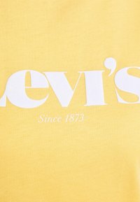 Žluté bavlněné tričko s velkým bílým logem "Levi's" a textem "Od 1873" pod ním. Hladký povrch s kulatým výstřihem.
