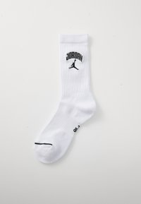Calcetín deportivo blanco con textura acanalada, que presenta un logo negro de "JORDAN" y una silueta de Jumpman en el puño, y una franja negra en la puntera.