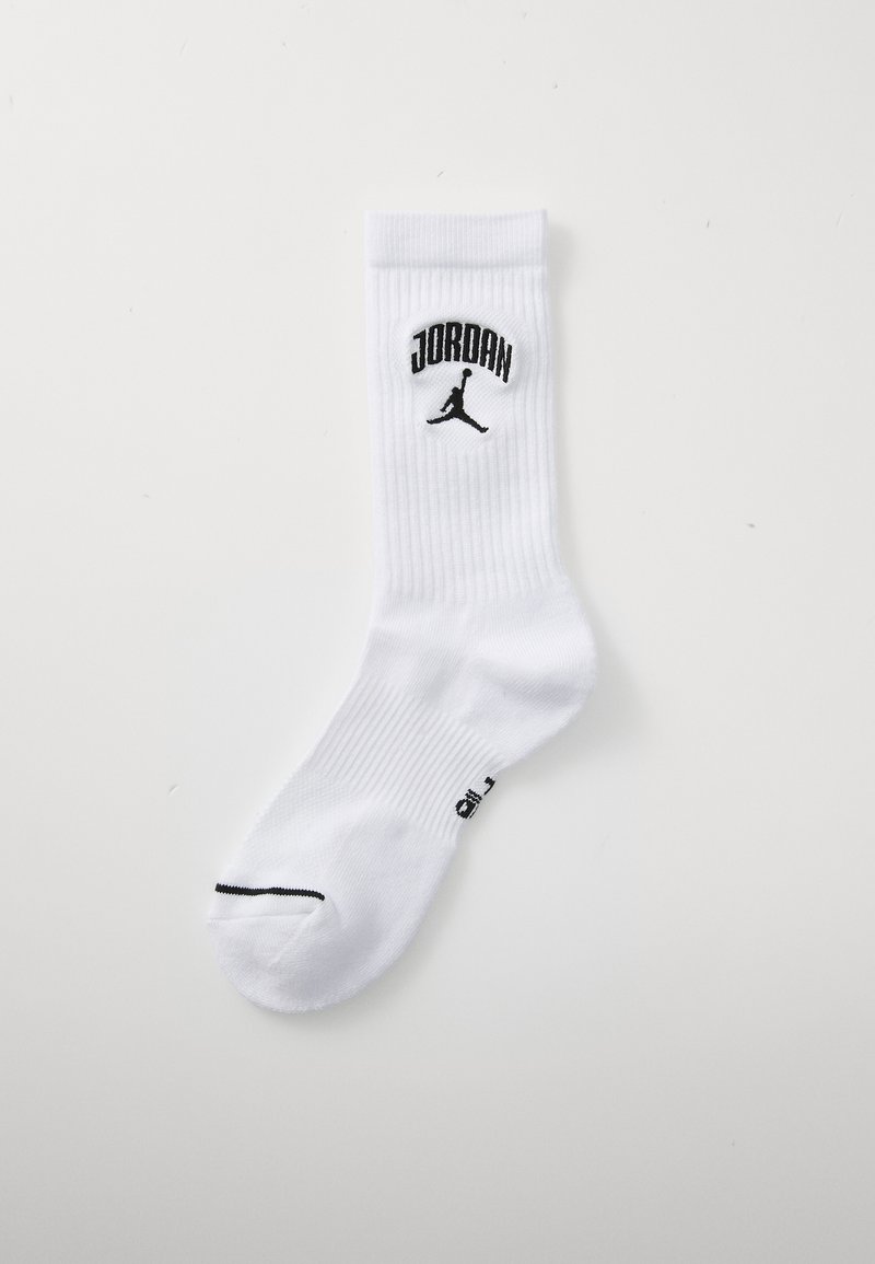 Baltas sporta zābaks ar ribotu tekstūru, uz kura ir melns "JORDAN" logotips un Jumpman siluets uz apkakles, kā arī melna josla uz pirksta.