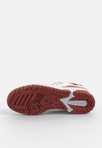 Semelle extérieure de sneakers blanche avec motif en caoutchouc rouge, un motif prononcé et le logo "New Balance". Texturée pour la traction et le soutien.