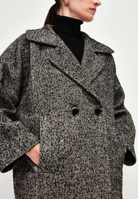 Cappotto in lana a motivo houndstooth con design doppiopetto, ampi revers, due tasche frontali e bottoni neri.