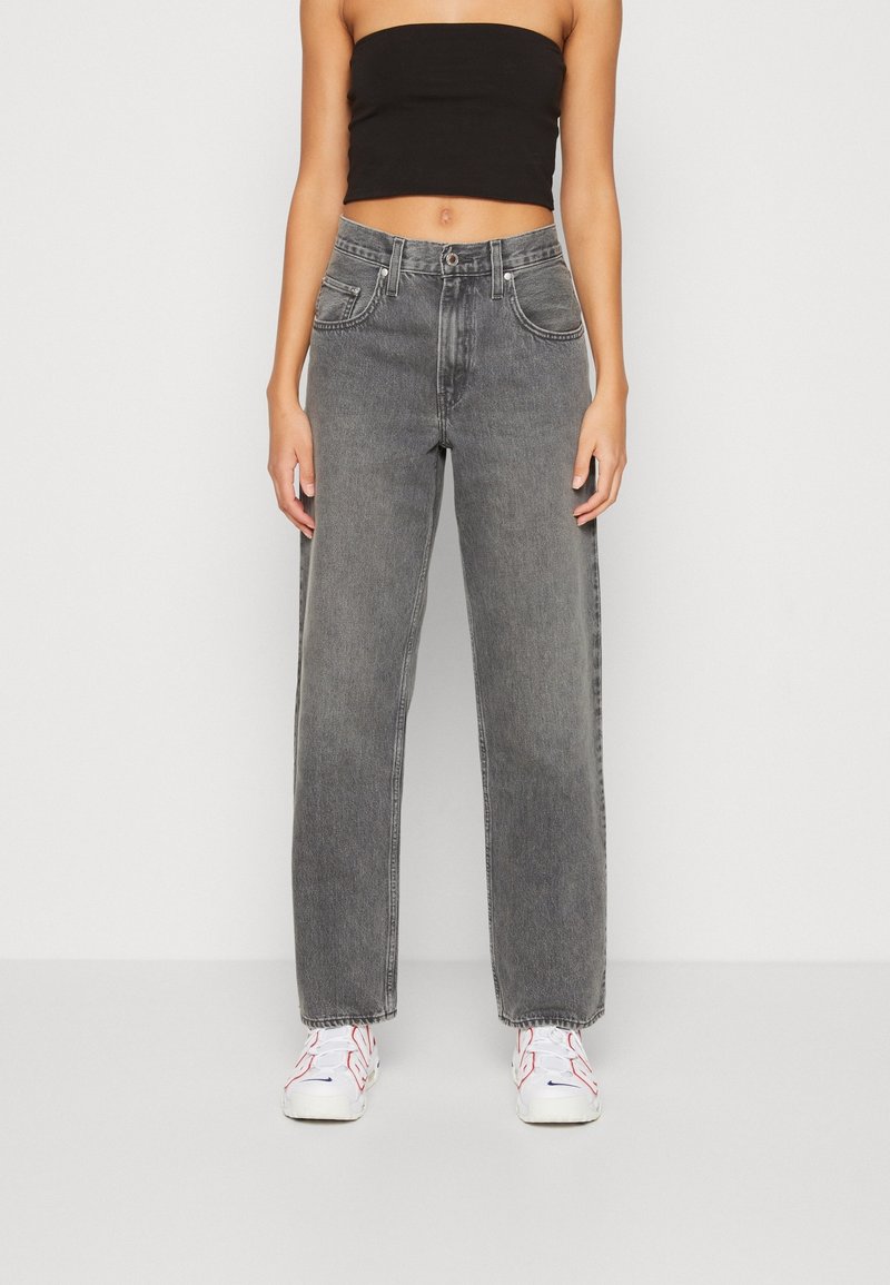 Jeans grigi alti in vita con taglio dritto, caratterizzati da un classico stile a cinque tasche e un leggero sbiadimento. Indossati con un top nero e sneakers bianche.