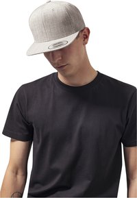 Hallhallane snapback müts, millel on lame ääre ja kuus paneeli, kantud veidi tahapoole musta lühikeste varrukatega T-särgi peal. Sile kangatekstuur.