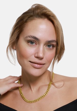 Collana in oro con un design spesso di anelli intrecciati. La superficie è lucida con una texture liscia. Indossata su un top nero.