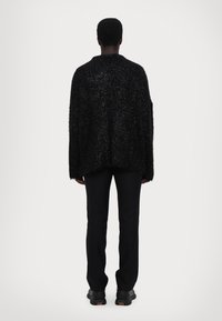 Pulover negru, pufos, supradimensionat, cu o croială lejeră, umeri lăsați și manșete ribbate, asortat cu pantaloni negri slim și pantofi negri.
