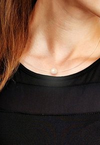 Duidelijke choker ketting met een enkele witte parel op een dunne, transparante koord. Draag tegen een zwarte top. Subtiel en minimalistisch ontwerp.
