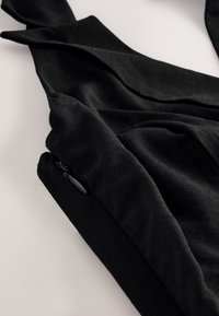 Gros plan sur une manche de vêtement noire avec une petite fermeture éclair noire et un tissu froncé sur un fond clair.