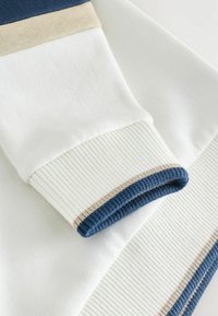 Witte sweatshirt met ribgebreide manchetten, voorzien van marineblauwe en beige strepen. Zacht materiaal met een gladde textuur.