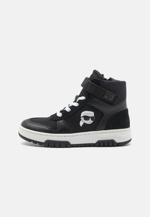 Baskets montantes noires avec semelle blanche, dotées d'un logo sur le côté, d'un laçage à l'avant et d'une sangle velcro ; fabriquées en cuir et en matériaux textiles.