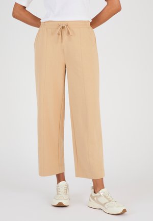 Persona vistiendo pantalones anchos cropped beige con costuras frontales, cintura elástica y cordones, combinados con zapatillas blancas y beige.