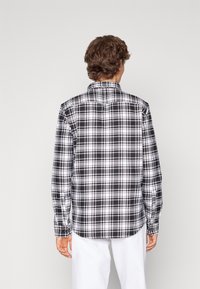 Camicia a maniche lunghe a quadratini bianchi e neri, con colletto a punta e polsini con bottoni, dal taglio rilassato e dettagli sullo yoke posteriore.