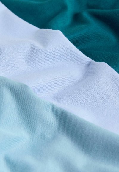 Tela de algodón con tres paneles de color: azul verdoso oscuro, blanco y turquesa claro. Textura suave con elasticidad visible y arrugas.