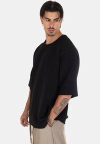 T-shirt oversize nero con un design testurizzato a costine e maniche larghe. Presenta un collo rotondo e una vestibilità rilassata, abbinato a pantaloni di colore chiaro.