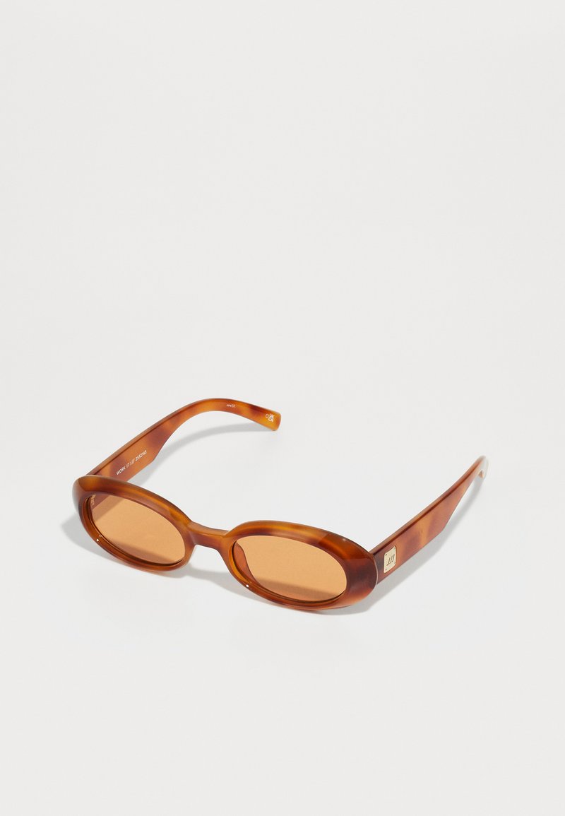 Brown tortoiseshell sunglasses with rounded lenses and thin, curved arms. Features light brown lenses and subtle metallic branding on the side.