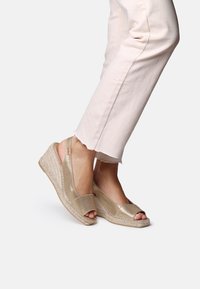 Goldene offene Keilabsatzsandalen mit einer gewebten Jute-Sohle und metallicfarbener Oberseite. Das Design verfügt über Slingback-Träger und eine glatte, glänzende Textur.