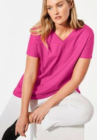 Kurzärmliges V-Ausschnitt-T-Shirt in leuchtendem Pink, aus weichem Stoff. Verfügbar in lockerem Schnitt, mit glatter Textur und ohne sichtbare Muster oder Verzierungen.