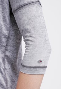 Camicia a maniche lunghe grigia con texture, con polsini arrotolati e piccolo logo in rosso, bianco e blu. Tessuto morbido e casual.