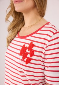 Gestreiftes T-Shirt in Weiß und Rot mit rundem Halsausschnitt, kurzen Ärmeln und strukturiertem roten Herz- Applikation mit besticktem Text darunter.