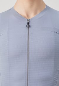 Maillot de cyclisme à manches courtes en gris clair avec un motif de grille texturé, doté d'une fermeture éclair à l'avant et d'un panneau de marque sur la poitrine.