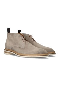 Beige suède enkelbootjes met bruin veter, een ronde neus en een witte zool met een tan accentband en een trekband aan de achterkant.