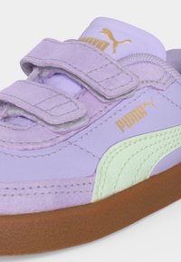 Αθλητικό παπούτσι Puma σε λιλά απόχρωση με δύο λουριά βέλκρο, χρυσό λογότυπο Puma, λευκή πλαϊνή ρίγα και καφέ λαστιχένια σόλα.