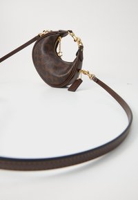 Borsa a tracolla in pelle marrone con una forma curvata, dotata di una zip, di hardware dorato e di una tracolla coordinata. Motivo sottile all'esterno.
