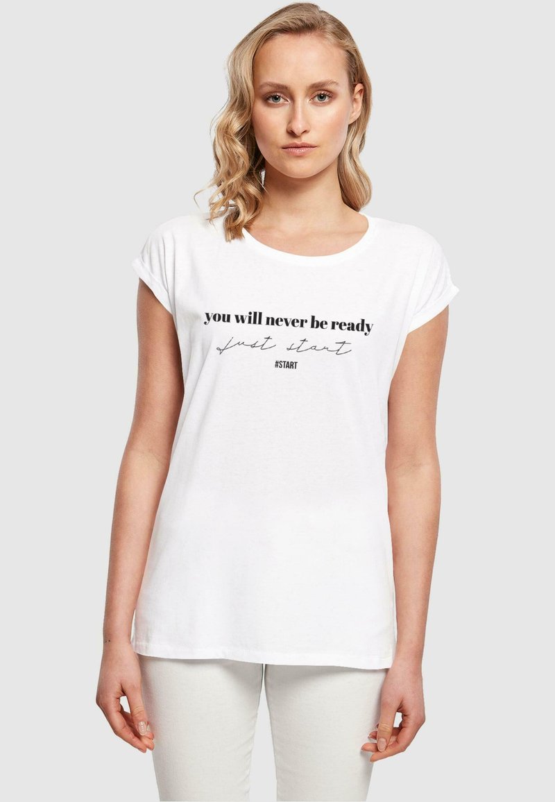 Hvid bomulds t-shirt med oprullede ærmer, der har sort tekst: "du vil aldrig være klar, bare begynd" og hashtag #START trykt på forsiden.