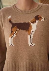 Brązowy sweter z dzianiny z motywem psa w kolorach białym, brązowym i beżowym, z prążkowanym dekoltem i dołem. Widoczna szczegółowa tekstura tkaniny.