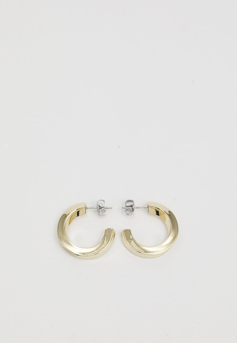 Złote metalowe kolczyki w kształcie kółek o gładkim, błyszczącym wykończeniu i częściowym okrągłym wzorze. Zamocowane na srebrnych zatyczkach i zapięciach.