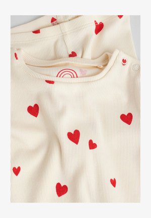 Top din material crem cu model nervurat și imprimeuri roșii de inimioare împrăștiate. Are un decolteu rotund și nasturi cu capse pe un umăr pentru îmbrăcare ușoară.