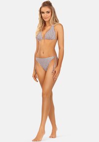 Wielokolorowy bikini z trójkątnym stanikiem i bokami wiązanymi. Tkanina ma geometryczny wzór z niebieskimi, czerwonymi i żółtymi akcentami.