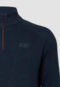 Donkerblauwe gebreide pullover met een half-rits kraag en geribbelde structuur, voorzien van een klein logo-opdruk op de borst.
