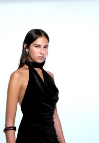 Svart halterneckklänning med drapering, figurnära silhuett och rynkdetaljer. Modellen bär ett vinrött armband och silverörhängen som accessoarer.