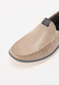 Beige læderslippersko med perforeret overdel, kontrasterende syninger, elastiske sidepaneler og en lys sål.