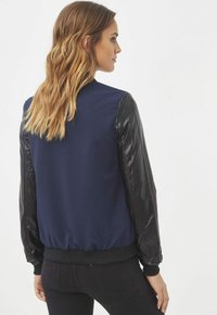 Chaqueta bomber navy con mangas de cuero negro, puños y cinturilla acanalados. Textura suave en las mangas, tejido texturizado en el cuerpo, diseño corto.