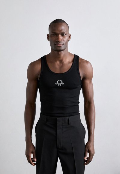 Top de tirantes negro con diseño ajustado, que presenta un pequeño logo bordado en el centro. Combinado con pantalones negros ajustados.