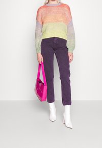 Mnohobarvý pletený svetr s oranžovými, levandulovými a zelenými pruhy, v kombinaci s fialovými džíny a lesklou růžovou kabelkou, doplněný bílými botami na blokovém podpatku.